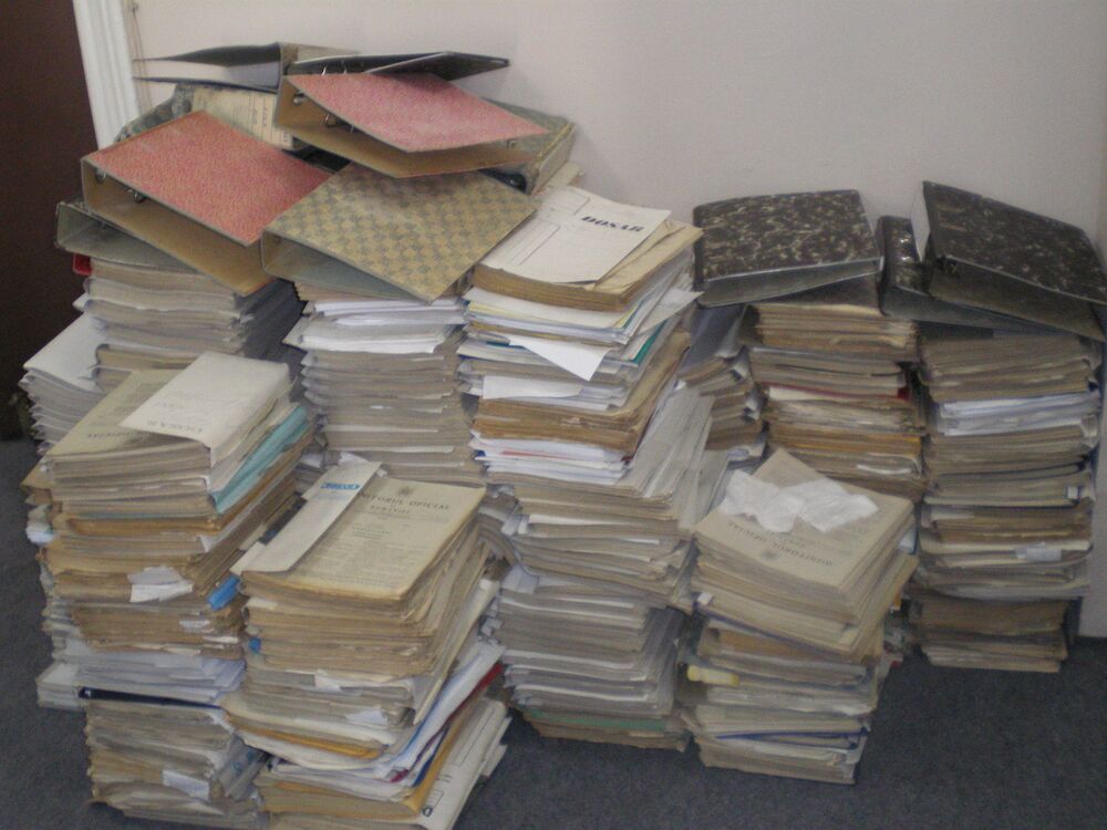 Montones de expedientes en papel apilados contra una pared