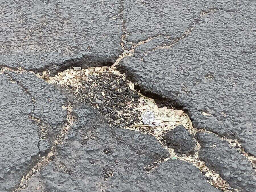 Bache abierto en el asfalto de una calle, con el pavimento agrietado alrededor